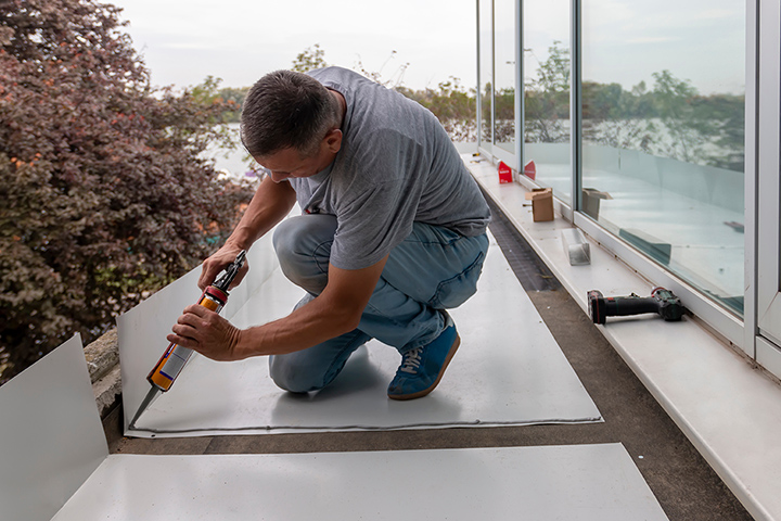 Man using sealant gun at roofing construction. Construction worker with silicone tube making roof waterproof
