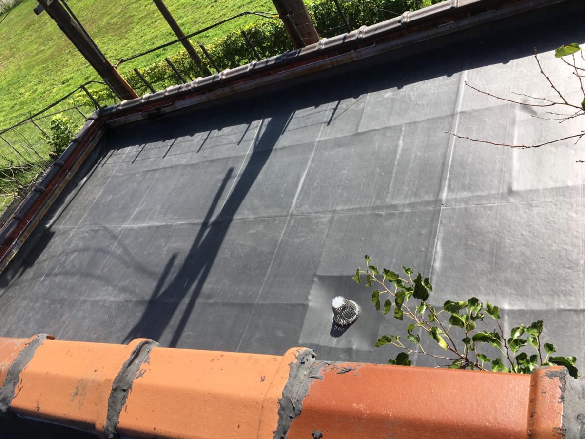 A black modified bitumen flat roof with a fallen tree branch on it. 