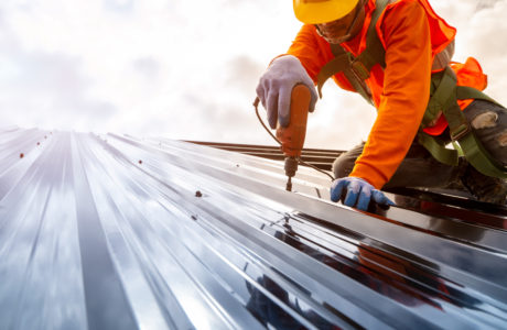 construction worker using electric drill to install a commercial steel roof