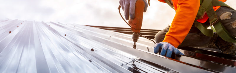 construction worker using electric drill to install a commercial steel roof