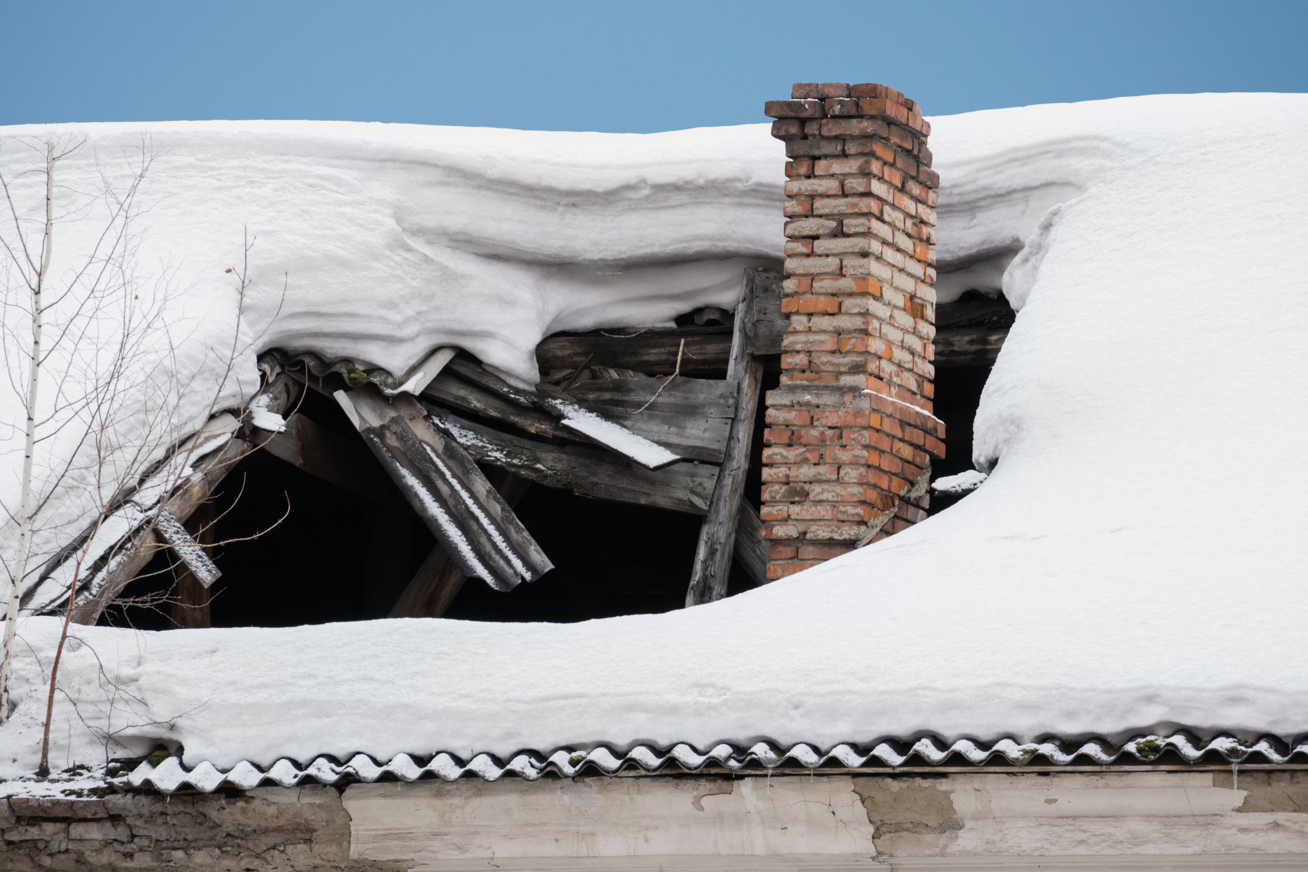Part of a house's roof has collapsed from snow buildup. There is a hole in the roof and the existing framing is broken. 