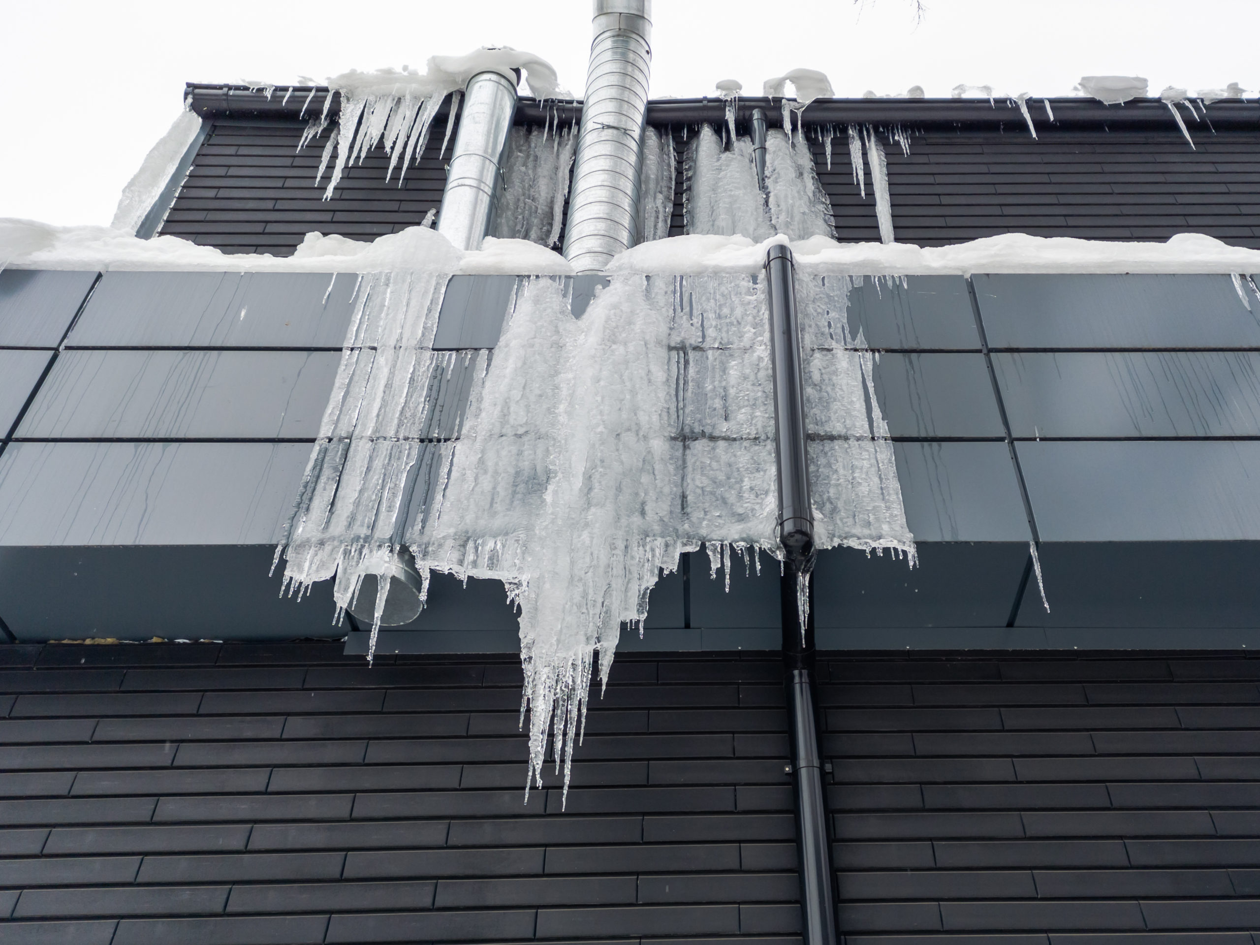 the side of a gray commercial building has large icicles hanging off of the gutters