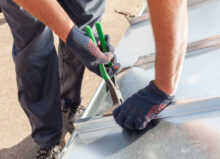 A roofer using pliers to fold and finish metal roofing