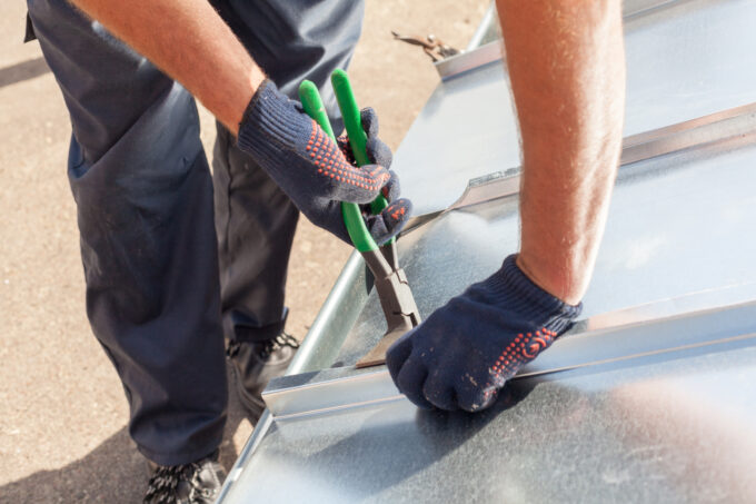 A roofer using pliers to fold and finish metal roofing