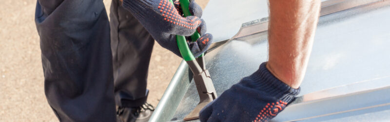 A roofer using pliers to fold and finish metal roofing