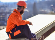 a roofer wears orange protective gear and holds a tool as he looks at a white flat roof