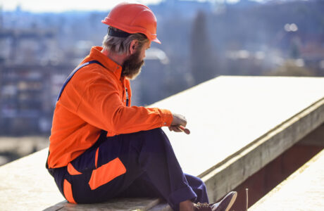 a roofer wears orange protective gear and holds a tool as he looks at a white flat roof