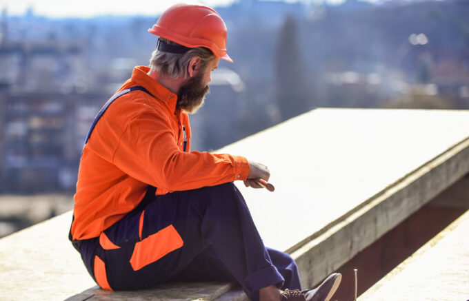 a roofer wears orange protective gear and holds a tool as he looks at a white flat roof